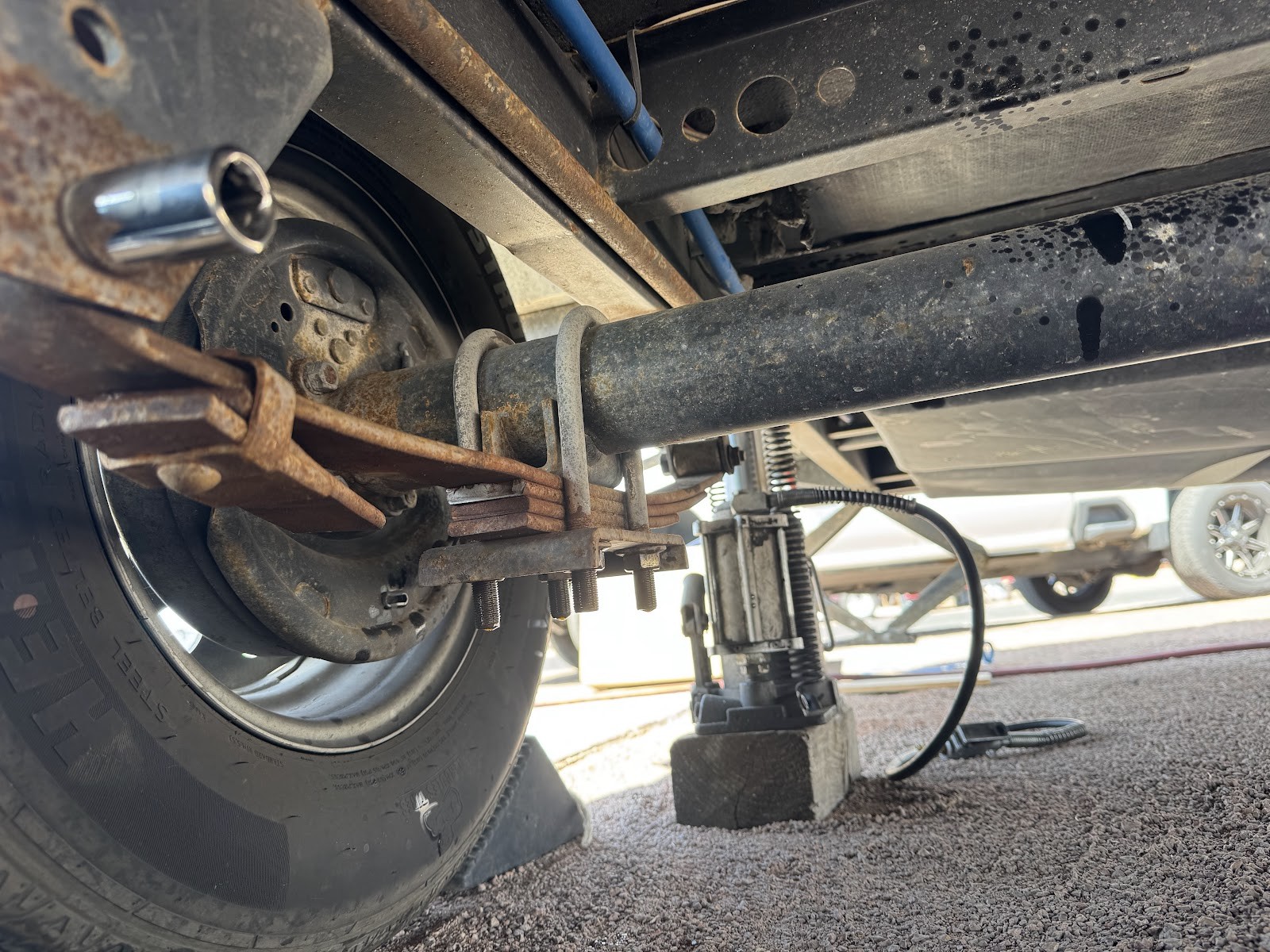 Underside of a trailer axle with leaf springs and a bottle jack during roadside service