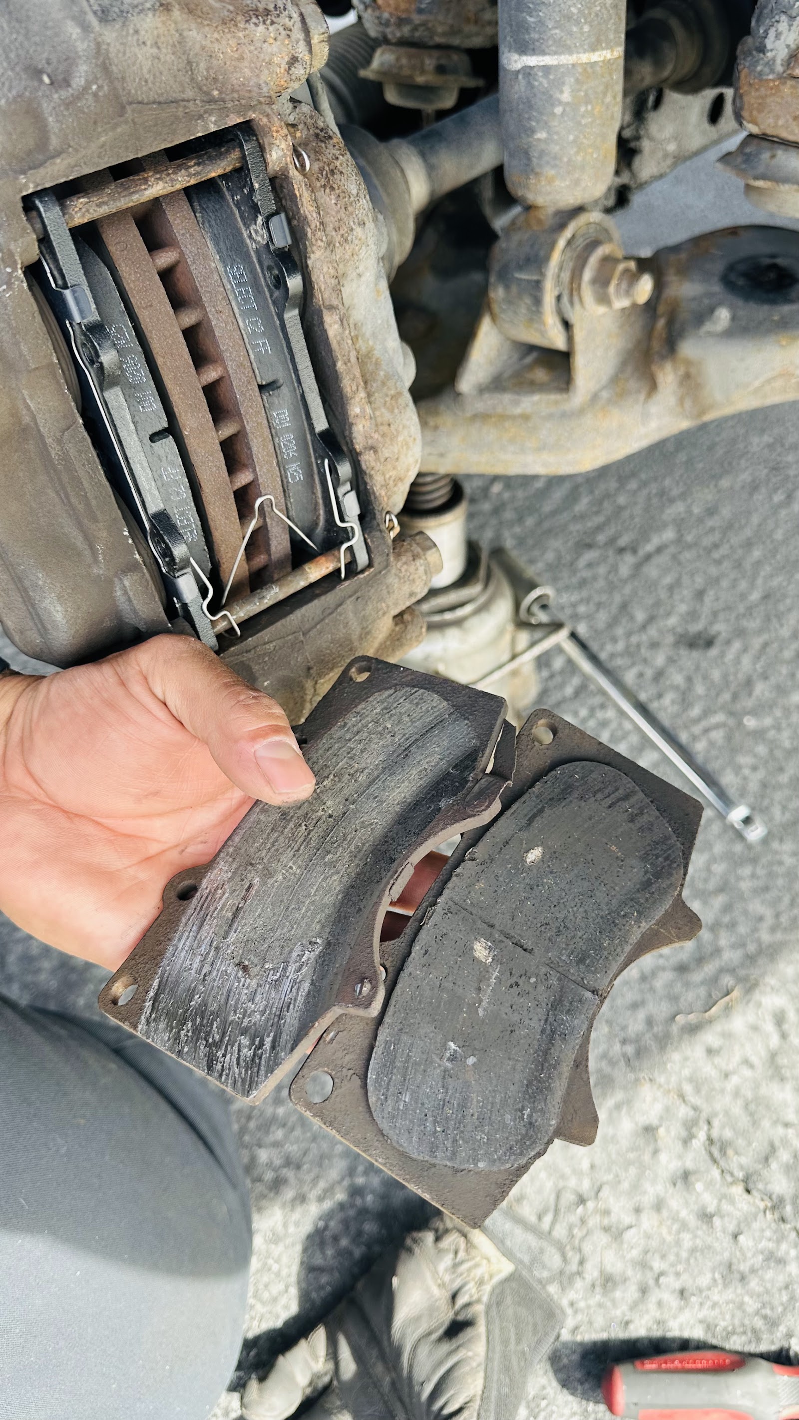 Mechanic holding worn brake pads next to a truck caliper during a brake job